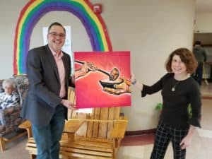 Kevin is donating an art piece to Julie at a senior center in Bellingham Washtington. There is a rainbow in the background.